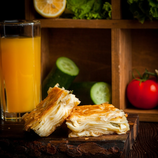 Free photo puff cheese cake with orange juice and cucumbers and tomato and lettuce in wooden plank