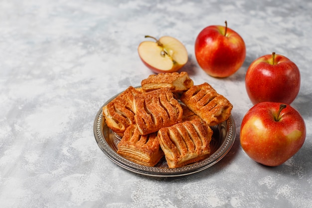 Puff pastry cookies filled with apple jam and fresh red apples on light concrete