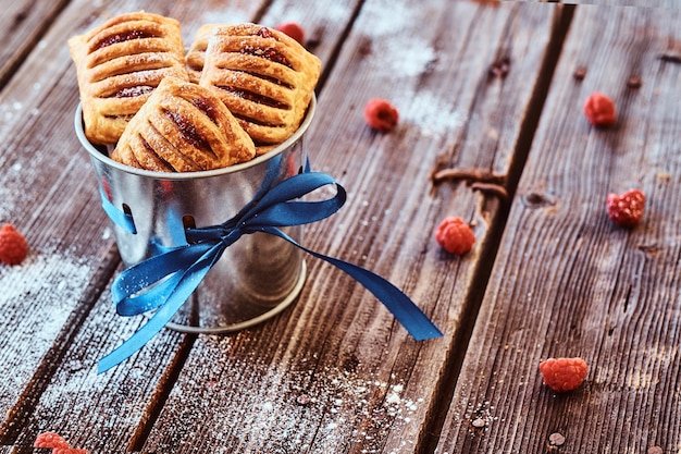 Puff pastry with jam in a bucket decorated with a blue ribbon on wooden boards with raspberries.