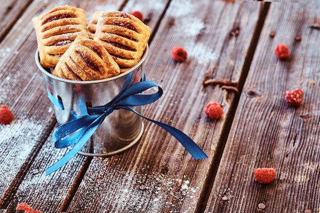 Puff pastry with jam in a bucket decorated with a blue ribbon on wooden boards with raspberries.