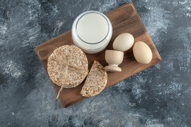 Puffed rice cakes, milk and eggs on wooden board