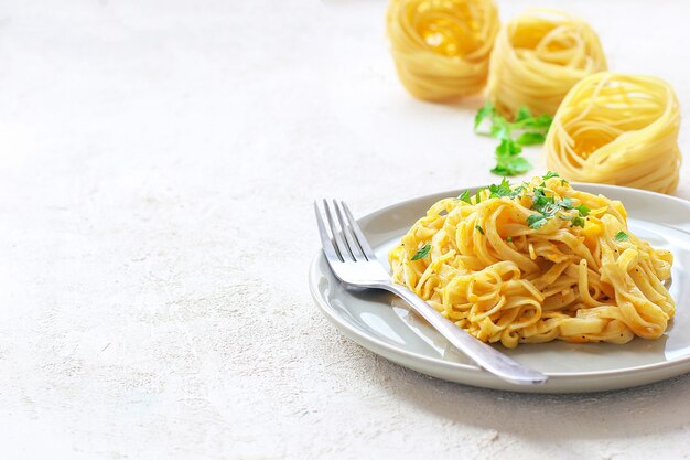 Pumpkin alfredo fettucine pasta in a ceramic plate with fresh raw butternut squash slices. Autumn meal for lunch. Butternut squash recipe.