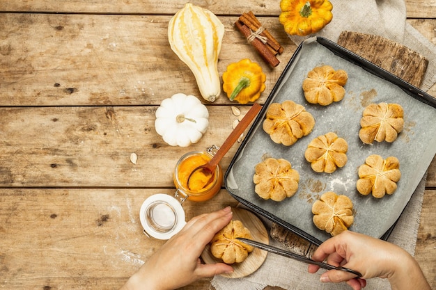 カボチャ​の​ロールパン​や​ビスケット​、​伝統的​な​秋​の​焼き​菓子​。​女性​の​手​は​クッキー​を​持っています​。​季節​の​自家製​料理​と​秋​の​装飾​。​古い​木​の​板​の​背景​、​上面図