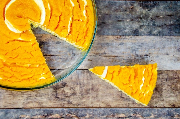 Pumpkin curd casserole. slice of pumpkin cheesecake next to platter of pie on wooden background