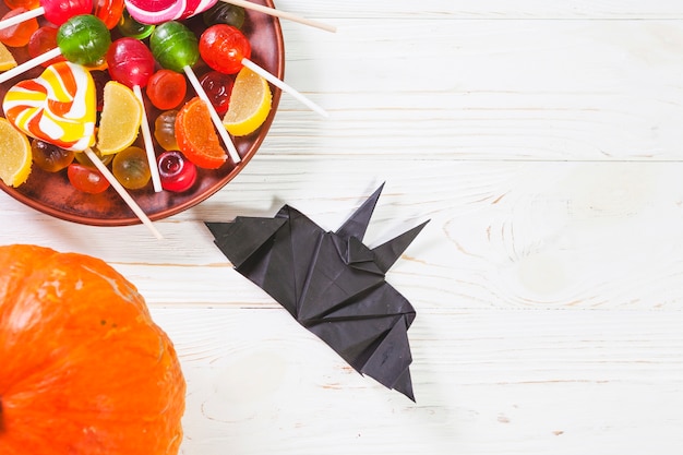 Pumpkin near bat origami and plate with bonbons