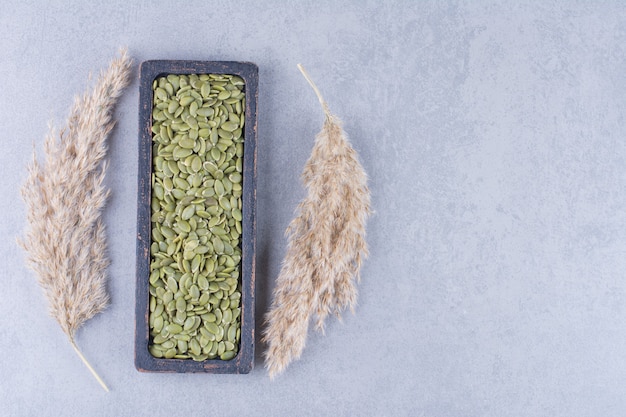 Бесплатное фото Тыквенное семя в деревянной тарелке рядом с травой пампасов на мраморе.