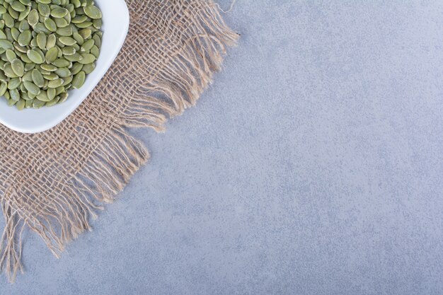 Pumpkin seeds in a bowl on a burlap napkin on the marble surface