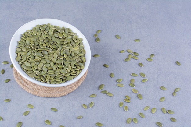 Free photo pumpkin seeds in a bowl on trivet on marble.