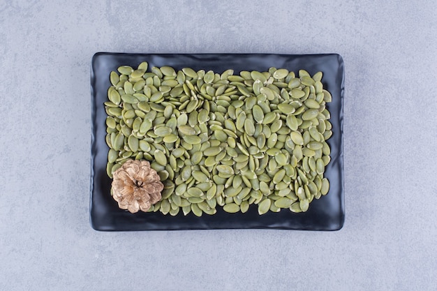 Pumpkin seeds and pine cone on platter on marble.