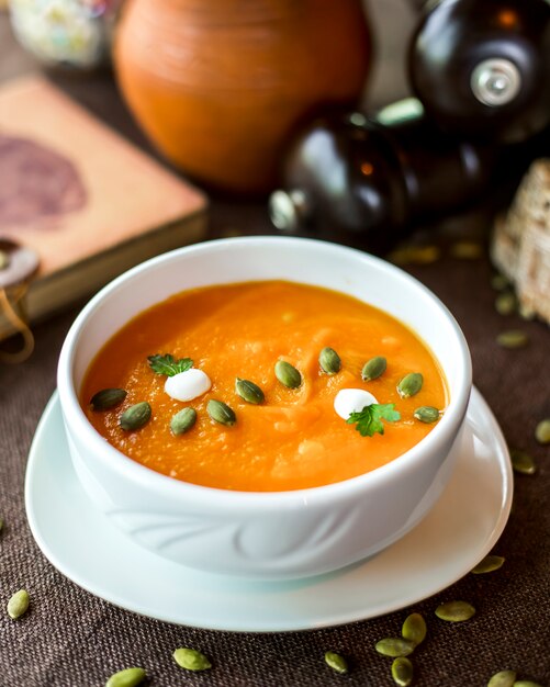 Pumpkin soup in the bowl cream seeds parsley side view