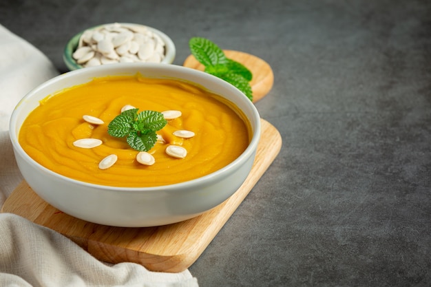 Pumpkin soup in white bowl placed on wooden cutting board