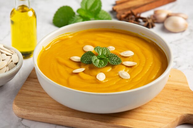 Pumpkin soup in white bowl placed on wooden cutting board