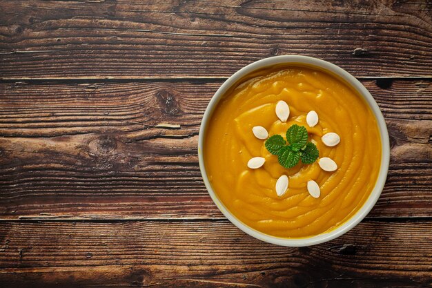 Pumpkin soup in white bowl placed on wooden floor