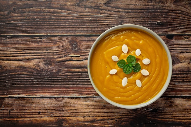 Pumpkin soup in white bowl placed on wooden floor