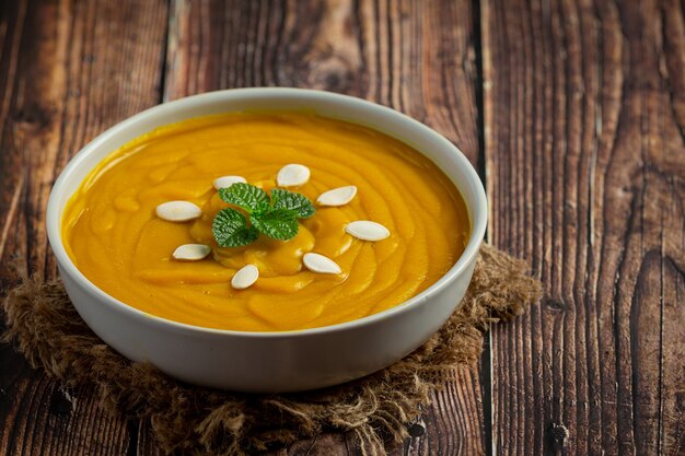 Pumpkin soup in white bowl placed on wooden floor