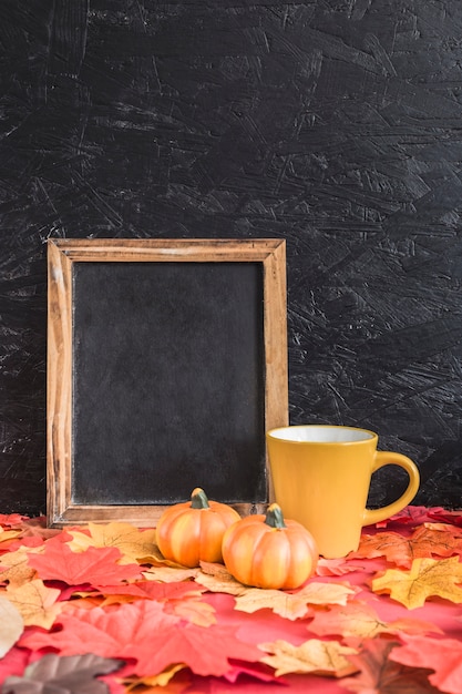 Pumpkins and mug near chalkboard on leaves