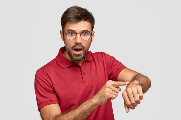 Punctual shocked man points at wrist, being very emotional checks time