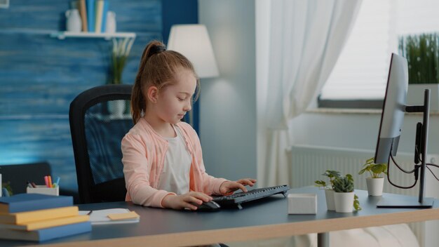 Ученик использует клавиатуру и компьютер для онлайн-уроков за партой. Молодая девушка смотрит на монитор для школьных заданий и домашних заданий. Маленький ребенок работает на компьютере для дистанционного обучения и знаний