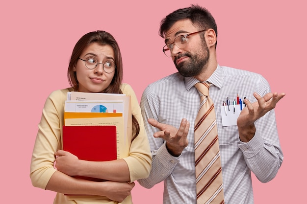 Free photo pupils of highschool have clueless expressions, look doubtfully at each other, cant decide on which topic to prepare course paper, stand next to each other