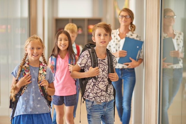 Free photo pupils and teacher walking across the corridor