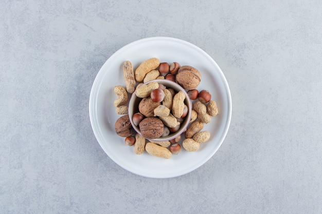 Purple bowl full of various shelled nuts on stone background.