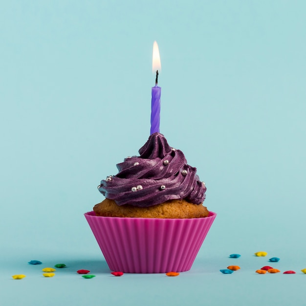 Purple burning candles on decorative muffins with colorful star sprinkles against blue backdrop