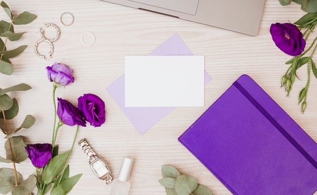 Purple eustoma flowers; earrings; rings; diary; wristwatch and nail polish on wooden desk