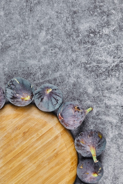 Purple figs around a wooden plate on marble.