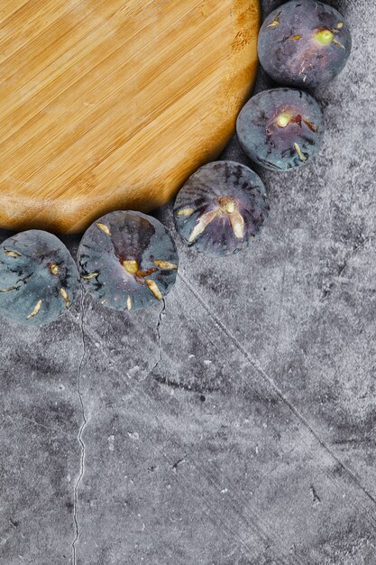 Free photo purple figs around a wooden plate on marble.