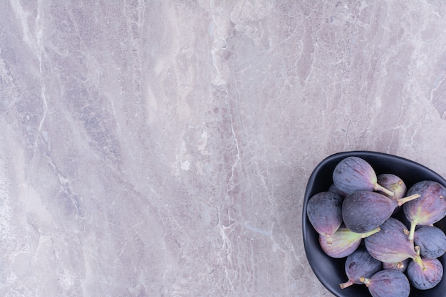 Purple figs in a black bowl on the marble