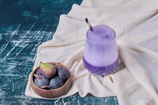 Purple figs with a cup of drink on blue.