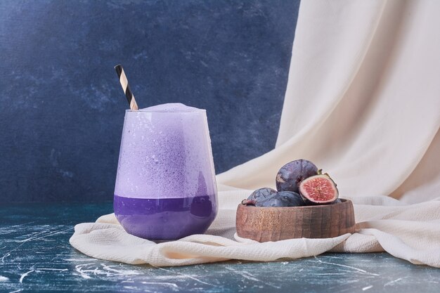 Purple figs with a cup of drink on blue.