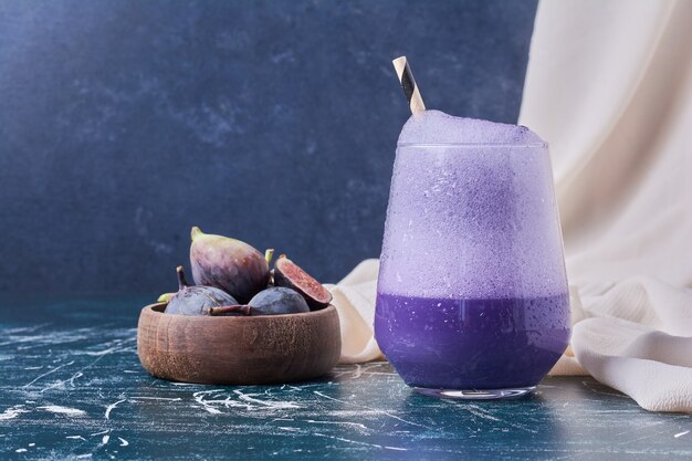 Purple figs with a cup of drink on blue.