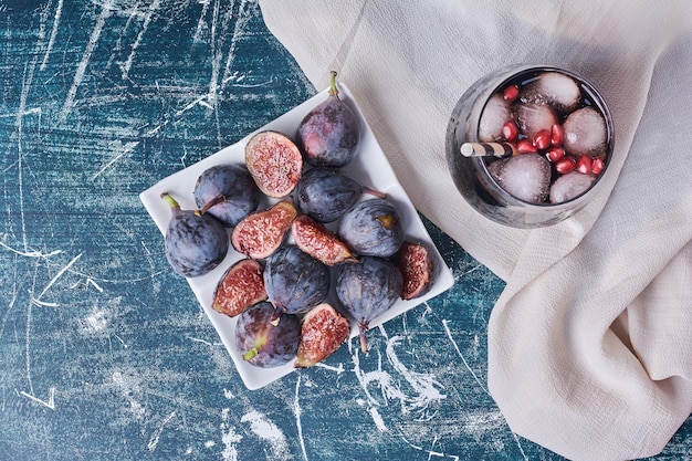 Purple figs with a cup of drink on blue.