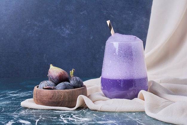 Purple figs with a cup of drink on blue.