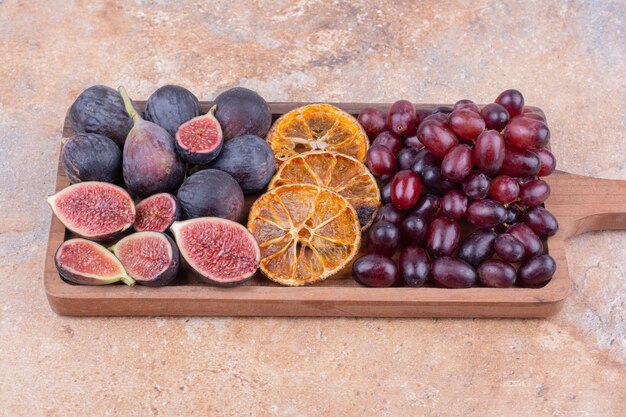 Purple figs with dry orange slices and cornel berries on a wooden board