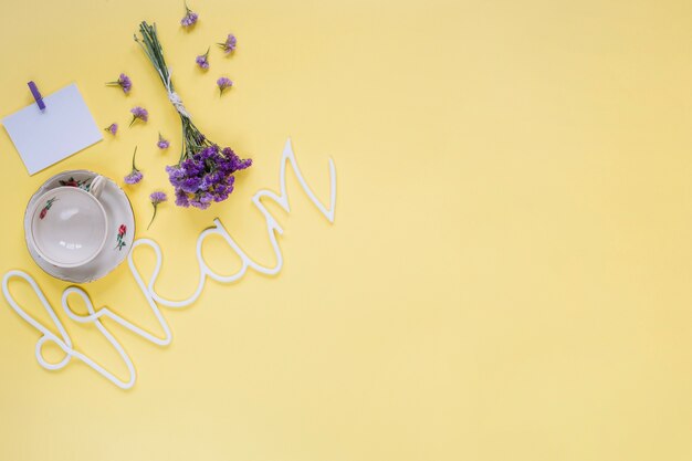 Purple flowers with dream word and empty cup on yellow surface