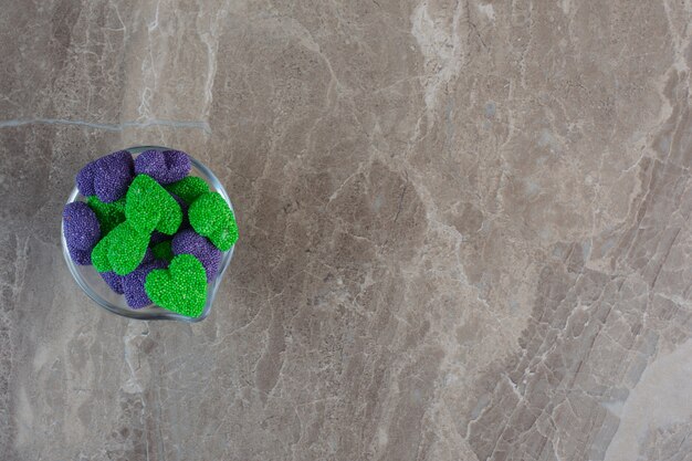 Фиолетовые и зеленые конфеты в форме сердца в стеклянной миске.