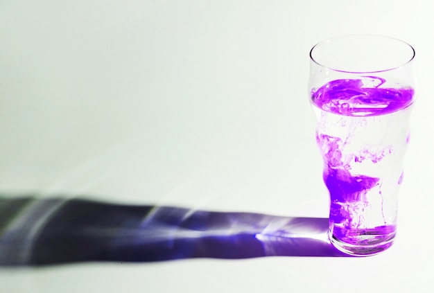 Бесплатное фото Фиолетовые чернила растворяются в стакане воды с тенью на белом фоне