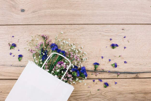 나무 책상에 흰색 쇼핑백 안에 보라색 리모 늄과 라든지 꽃