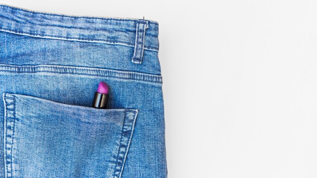 Фиолетовая помада в кармане синих джинсов на белом фоне