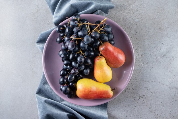 Purple plate of black grapes and tasty pears on stone background. 