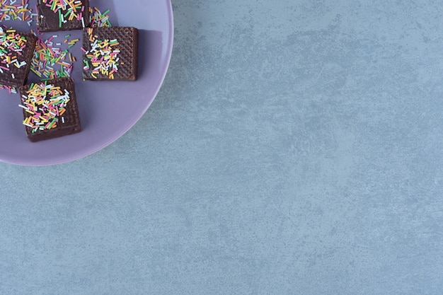 Purple plate on the corner. Chocolate wafers with sprinkle on plate.