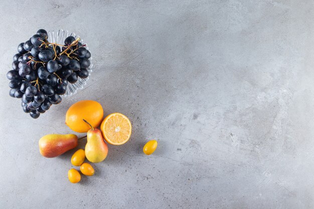 Purple plate of fresh black grapes and pears on stone background. 