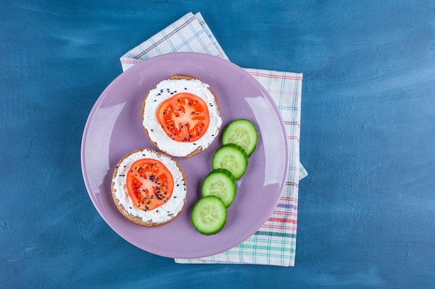 A purple plate of sliced cucumber and sandwiches with cheese and sliced tomato .