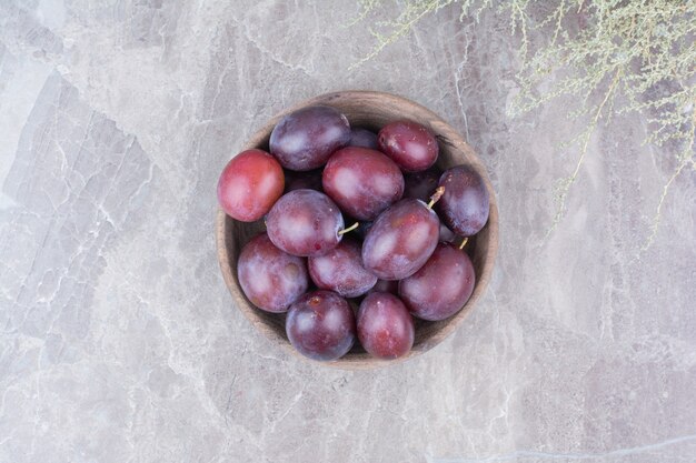 Purple plums in wooden bowl on stone background. 