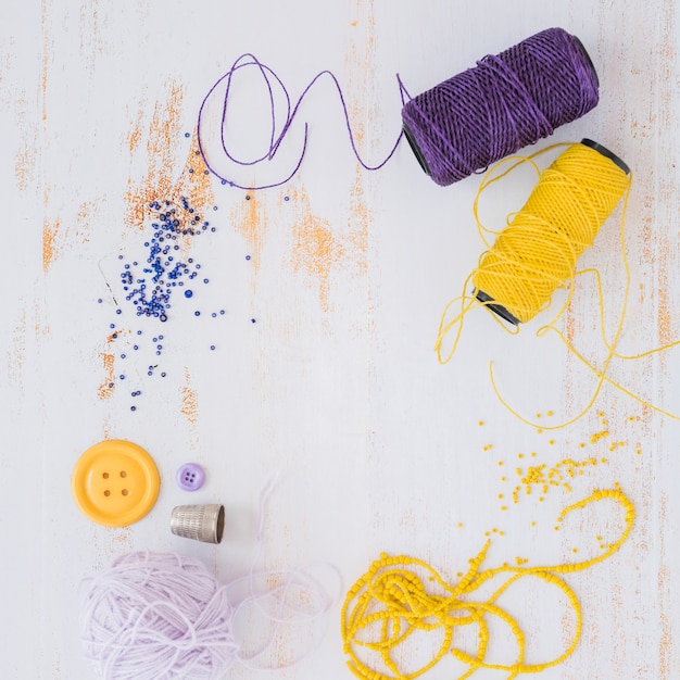 Free photo purple and yellow yarn ball; button with beads on white wooden textured backdrop