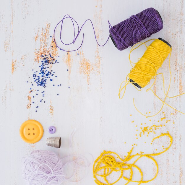 Purple and yellow yarn ball; button with beads on white wooden textured backdrop