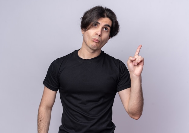 Pursing lips young handsome guy wearing black t-shirt points at up isolated on white wall