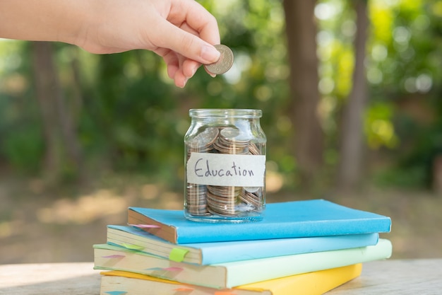 Putting money coins saving in glass bottle for concept investment mutual fund finance and business, placed on the textbook. content money saving for education.